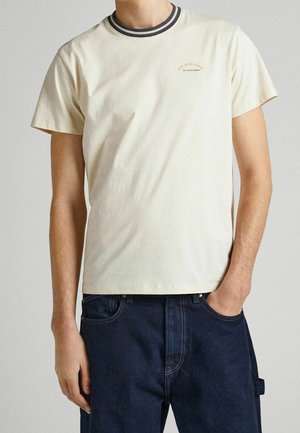 Mann trägt ein offwhite T-Shirt mit kurzen Ärmeln, gestreiftem Kragen und kleinem „Pepe Jeans London“-Logo, kombiniert mit dunkelblauen Jeans.