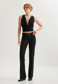 Top senza maniche nero con scollatura profonda, abbinato a pantaloni neri su misura e décolleté a punta, caratterizzato da una silhouette elegante e aderente.