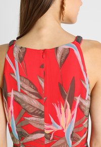 Rød blomstermønstret kjole med lynlås bagpå og udsmykkede skulderstropper. Stoffet har en glat overflade med fremtrædende farver.