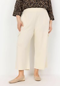Cream-colored wide-leg pants, featuring side pockets and a smooth texture, paired with beige flats having a perforated design.
