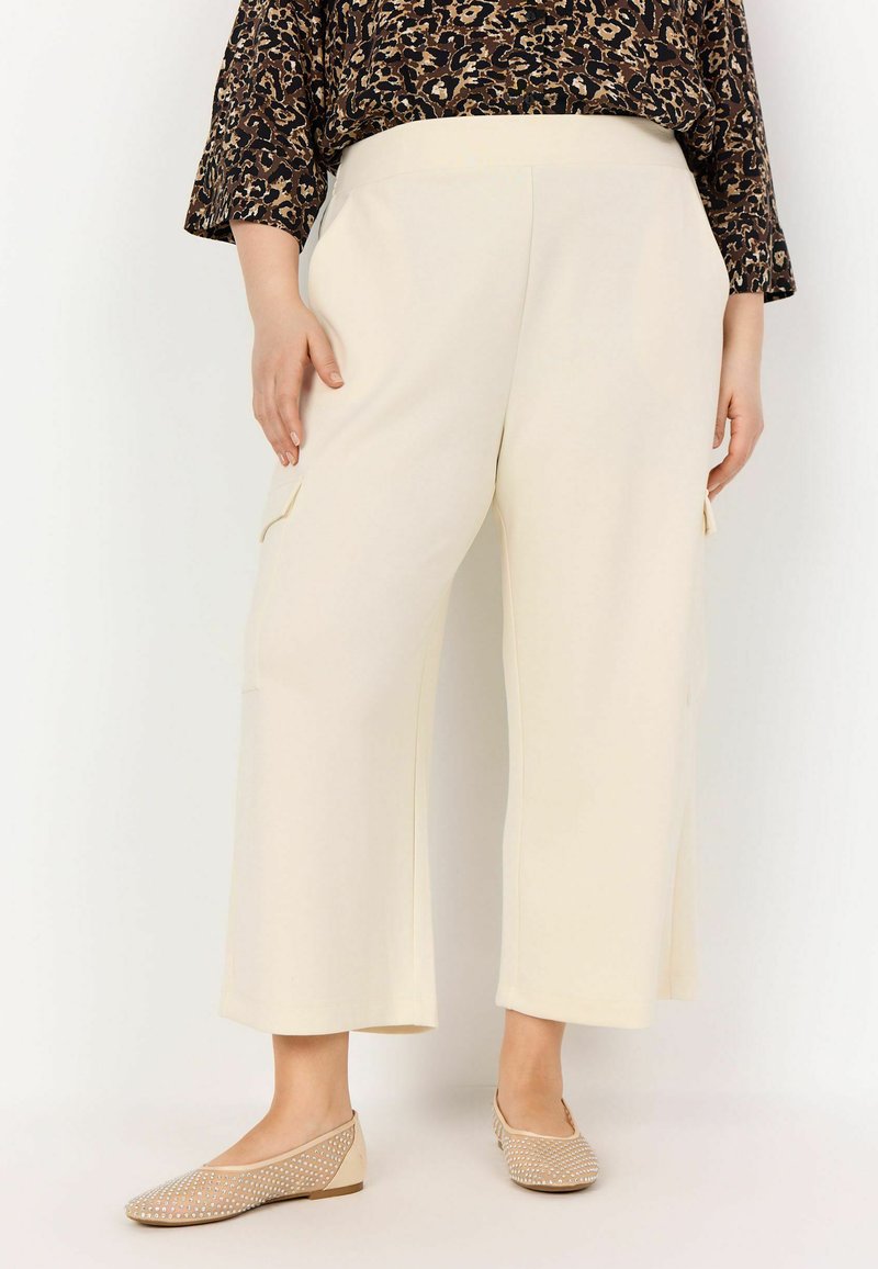 Cream-colored wide-leg pants, featuring side pockets and a smooth texture, paired with beige flats having a perforated design.