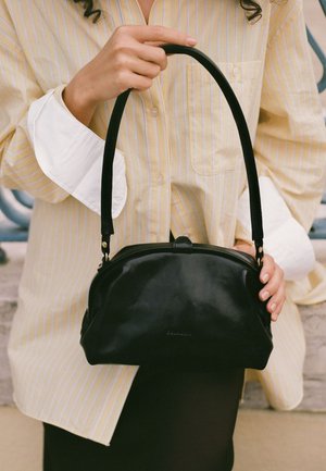 Borsa a mano in pelle nera con forma curva, dotata di manico corto e dettagli in metallo dorato. La borsa ha una texture liscia e un marchio discreto.