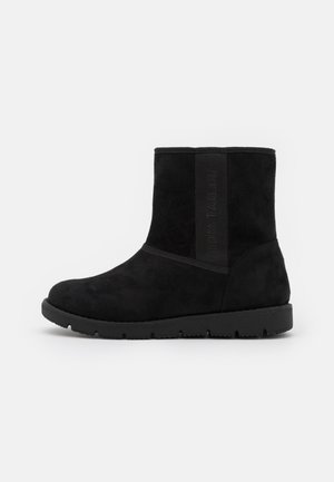 Des bottines en daim noir avec un bout arrondi, une semelle en caoutchouc plate et un panneau élastique sur le côté avec le nom de la marque embossé.