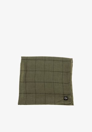 Tovagliolo di stoffa verde oliva con un sottile motivo a griglia nera, piegato ordinatamente e un piccolo etichetta nera con logo bianco nell'angolo.