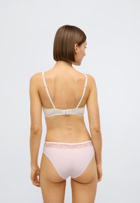 Béžová podprsenka s nastavitelnými ramínky a zapínáním na háček, doplněná světle růžovými kalhotkami s krajkovým zdobením v pase. Hladká textura.