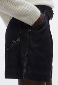 Temno modri kratki hlače iz jeansa s prilegajočo se silhueto, s kontrastnim rumenim šivom in žepom z diskretno blagovno znamko.