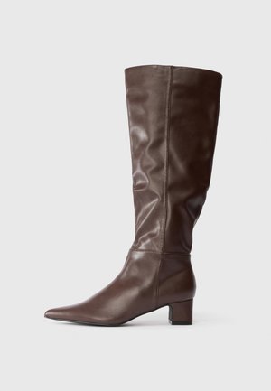 Høj brun læderstøvle med en lav blokhæl og et let rynket lægområde, vist i profil på en hvid baggrund.