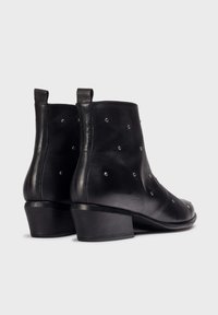 Black leather ankle boots with a pointed toe, adorned with silver studs, featuring a low block heel and pull tabs at the back.