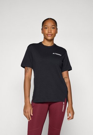 T-shirt noir à manches courtes avec col rond et logo TERREX en blanc. Tissu doux, coupe décontractée, fentes latérales, associé à des leggings bordeaux.