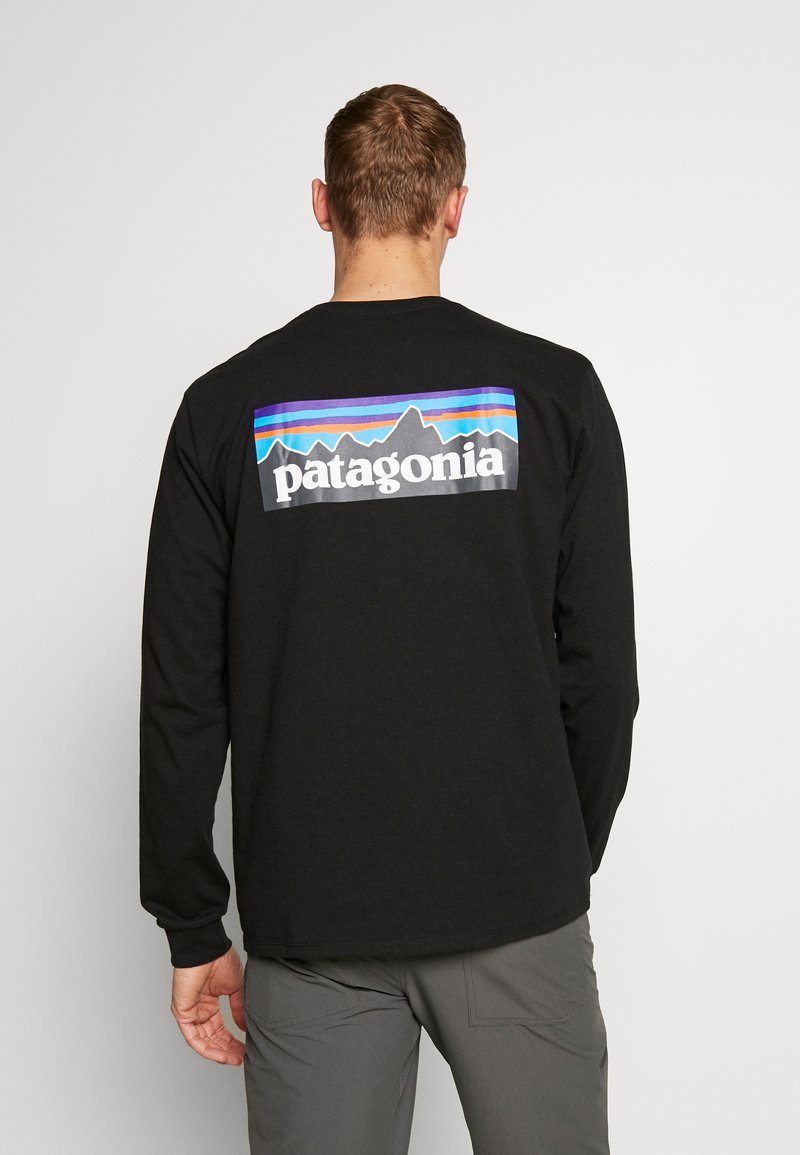 Sort langærmet skjorte med grafisk design på ryggen, som viser "patagonia" og farverige bjergkonturer. Bomuldsstof.