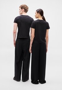 T-shirts pretas de manga curta combinadas com calças pretas largas e soltas. Design minimalista com acabamento em tecido macio. Vista traseira lisa.