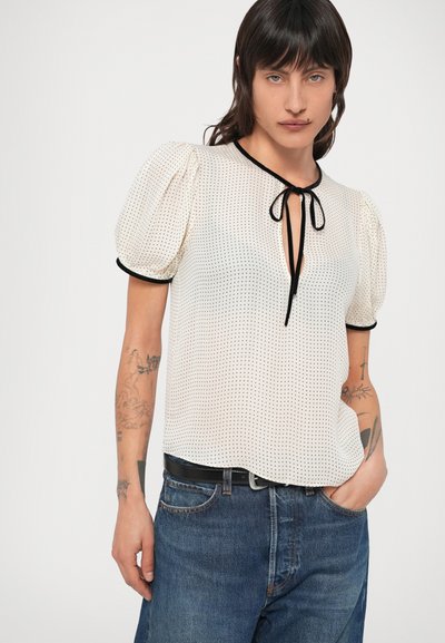 Vit blus med svarta prickar, puffärmar, V-ringning med knytband och svart kant. Kombinerad med blå jeans i denim.