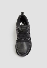 Scarpa sportiva nera con superiore in rete e sintetico, superficie testurizzata, chiusura con lacci e logo sulla linguetta. Presenta una suola in gomma nera solida.