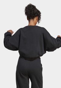 Beskuren svart sweatshirt med lösa, långa ärmar och rund halsringning. Mjuk textur, minimala sömnadsdetaljer, bärs med matchande svarta byxor.