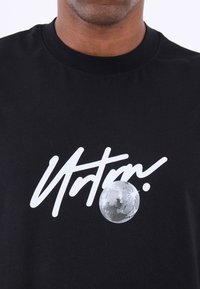 Svart t-shirt i bomull med fet vit text "Ultra" och en discokula-grafik, rund halsringning och korta ärmar.