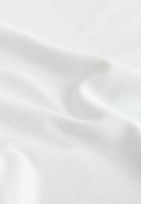 Tissu blanc lisse avec des plis doux et des ombres délicates, mettant en valeur la texture et la chute du matériau.