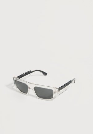 Ορθογώνια γυαλιά ηλίου με διάφανα πλαίσια, σκουρόχρωμους φακούς και μαύρο κείμενο στο μήκος των βραχιόνων πάνω σε λευκό φόντο.