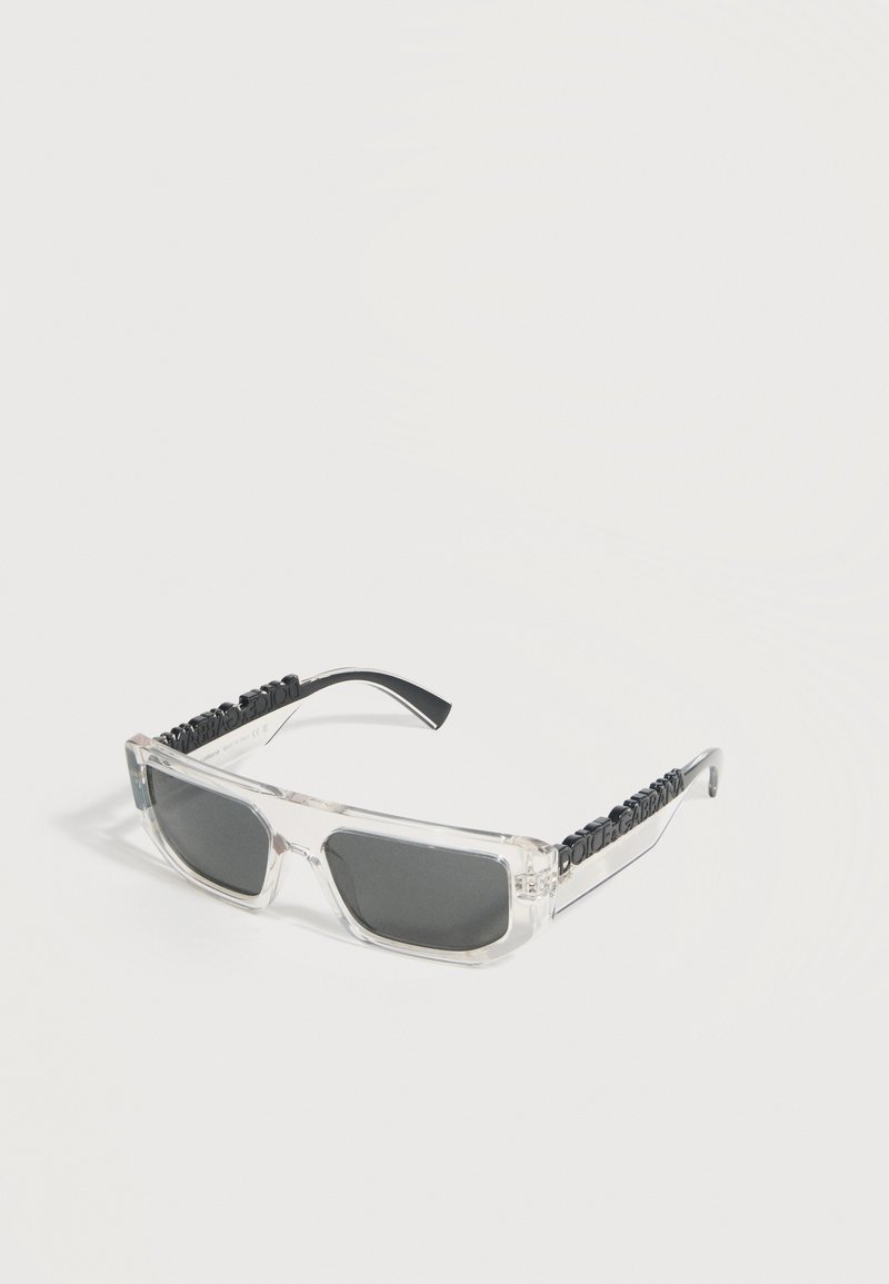 Ορθογώνια γυαλιά ηλίου με διάφανα πλαίσια, σκουρόχρωμους φακούς και μαύρο κείμενο στο μήκος των βραχιόνων πάνω σε λευκό φόντο.