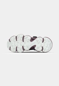 Semelle de chaussure avec une semelle extérieure blanche, des accents violets et un motif de préhension texturé. Présente un design à plusieurs couches avec un marquage de marque visible.