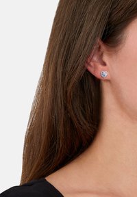 Pendientes de stud en forma de corazón en azul y plata, con un acabado brillante. Montados en un soporte estándar para pendientes.