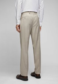 Beige maßgeschneiderte Hose mit geradem Schnitt, Rückentaschendetails und subtiler Textur. Kombiniert mit einem weißen Langarmhemd und dunklen Schuhen.