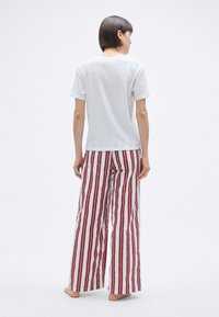T-shirt blanc associé à un pantalon large à rayures rouges et blanches en tissu léger, avec une coupe ample et un design décontracté.
