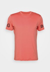 T-shirt corail à manches courtes en tissu lisse. Il présente un col rond et des lettres noires sur la manche gauche. Design simple et ajusté.