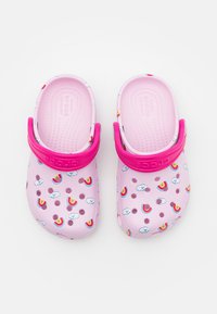 Różowe klapki wykonane z gumy z paskiem, zdobione wzorem tęczy i chmur, z teksturowanym wkładem oraz otworami odpływowymi.