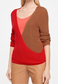Pull en tricot avec un design asymétrique et un décolleté en 'V' profond, rouge d'un côté et marron de l'autre, avec des poignets côtelés et une coupe décontractée.