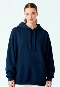 Hanorac cu glugă de culoare bleu marin, realizat dintr-un material moale, având o buzunar frontal, șnururi ajustabile și manșete ribbate. Croială lejeră cu umeri relaxați.