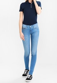 Námořnický polo tričko se třemi knoflíky, fitted silueta. Světle modré skinny džíny, střední pas, měkký denim. Černé tenisky s bílými tkaničkami.