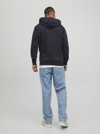 Helle sweatshirt in Marineblau mit entspannter Passform, kombiniert mit hellblauen Jeans. Das Outfit wird mit weißen Sneakern abgerundet.