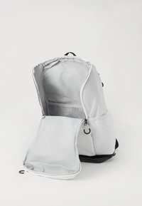 Sivý látkový batoh s hlavnou priehradkou na zips, sieťovanou kapsou a čiernym dnom. Obsahuje prednú kapsu so klopou a háčik.