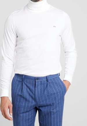 Weißer Langarm-Turtleneck, figurbetontes Design, weiche Textur; kombiniert mit blauen, feingestreiften Hosen mit vorderen Falten und Knopfverschluss.