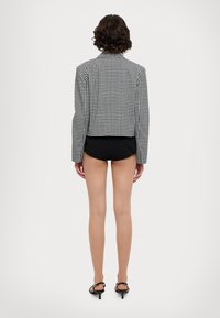 Blazer cropped a scacchi bianco e nero con maniche lunghe, spalle strutturate e orlo dritto, abbinato a pantaloni corti neri e tacchi.