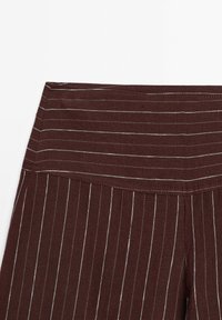Burgundifärgade byxor med hög midja har tunna vita vertikala ränder. Mjuk textur med plisserad design i tyget.