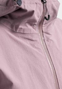 Close-up of a light mauve jacket with a visible front zipper and adjustable hood drawstring with black plastic toggle.