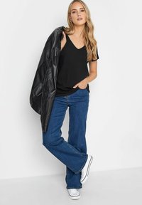 Musta V-paitapusero, yhdistettynä sinisiin leveisiin farkkuihin ja valkoisiin lenkkareihin. Musta nahkatakki on heitetty yhden olkapään yli.