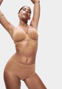 Sostenedor sin costuras de color nude, acolchado, con tirantes ajustables y braguita de tiro alto. Tela suave y elástica con un diseño sin costuras para mayor comodidad.