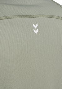 Olivgrön träningslinne med ribbat mönster. Har en vit chevronlogga nära halsringningen och sömmar längs kanterna.