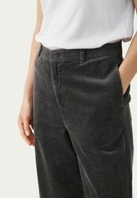 Harmaat corduroy-housut, joissa on pystyribbaus, sivutaskut ja suora malli, yhdistettynä yksinkertaiseen valkoiseen paitaan rentossa ympäristössä.