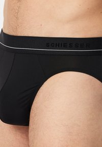 Sorte bomuldsunderbukser med elastisk talje, der har hvid kant og prægede "Schiesser"-mærkning. Glat tekstur, tætsiddende design.