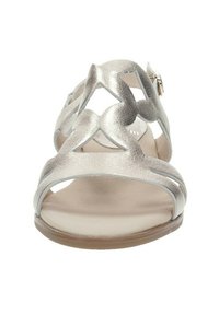Sandal de color plateado metálico con diseños florales recortados, suela plana y correa ajustable en el tobillo. Textura suave con un perfil bajo.