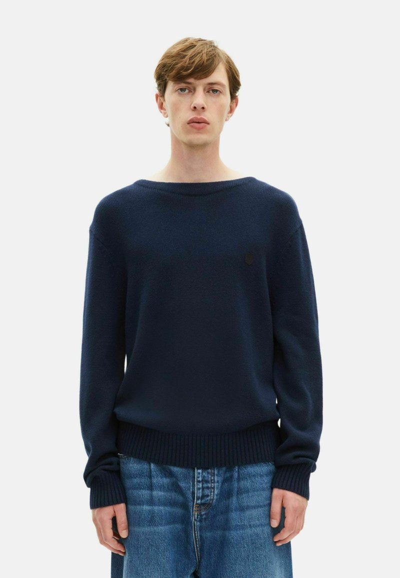 Marineblauer Strickpullover mit weitem Rundhalsauschnitt, gerippten Bündchen und Saum, der ein kleines Emblem auf der Brust trägt. Lässige Passform für zusätzlichen Komfort.