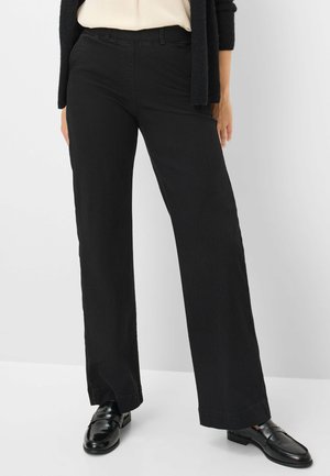 Schwarze weite Baumwollhosen mit Reißverschluss, Gürtelschlaufen und einem schlichten Design. Kombiniert mit schwarzen Slippern.