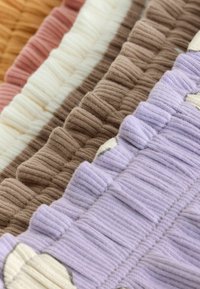 Gros plan d’un tissu tricoté côtelé dans des couleurs pastel superposées : lavande, beige, blanc, rose doux et jaune moutarde.