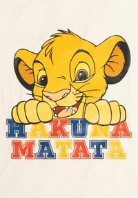 Leone cartonato giallo con grandi orecchie che sbircia sopra il testo "HAKUNA MATATA" in lettere blu, rosse e gialle su uno sfondo chiaro.