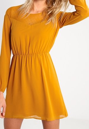 Musztardowożółta sukienka z długimi rękawami, teksturowanym wzorem kropek na gorsecie, elastyczną talią i rozkloszowaną, lekką spódnicą.