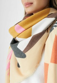 Écharpe texturée présentant des formes abstraites en jaune, rose, gris et marron sur un fond beige. Tissu doux avec des bords effilochés.