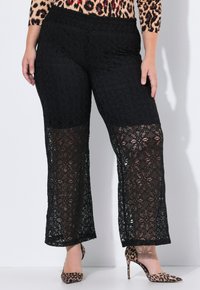Zwarte gehaakte kanten broek met een wijdvallende snit, voorzien van bloemmotieven en een effen tailleband. Gecombineerd met loafers in luipaardprint.